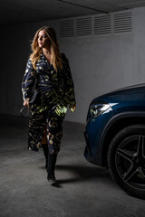 Elegantly dressed blonde woman walking beside a car at night in a garage