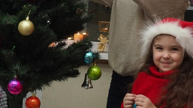 Family decorating a Christmas tree with boubles in the living room. mom and daughter decorate the tree with different toys home, family holidays, happy new year and christmas