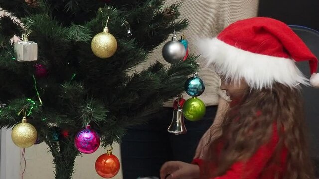 Family decorating a Christmas tree with boubles in the living room. mom and daughter decorate the tree with different toys home, family holidays, happy new year and christmas