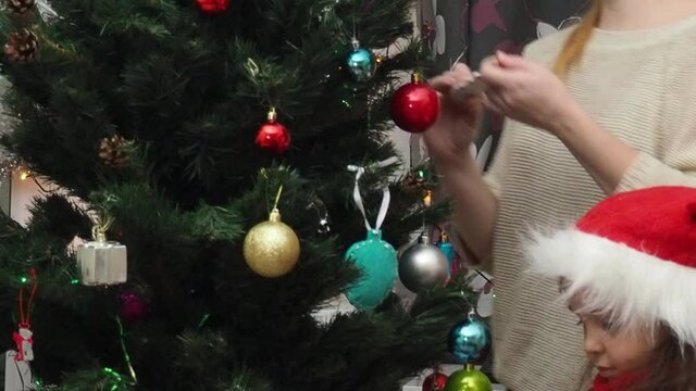 Family decorating a Christmas tree with boubles in the living room. mom and daughter decorate the tree with different toys home, family holidays, happy new year and christmas