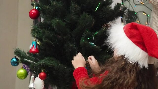Family decorating a Christmas tree with boubles in the living room. mom and daughter decorate the tree with different toys home, family holidays, happy new year and christmas