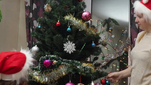 Family decorating a Christmas tree with boubles in the living room. mom and daughter decorate the tree with different toys home, family holidays, happy new year and christmas