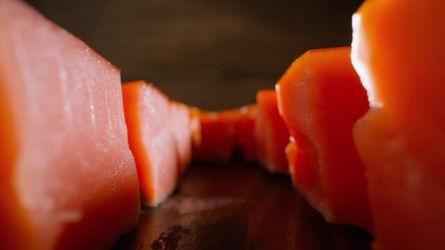 Motion between lines of tasty natural red cool smoked pink salmon cubes lying on rustic wooden table at bright light extreme closeup slow motion