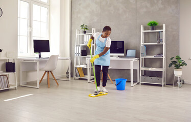 African American woman janitor with mop clean office floor with sanitizer liquid detergent. Black...