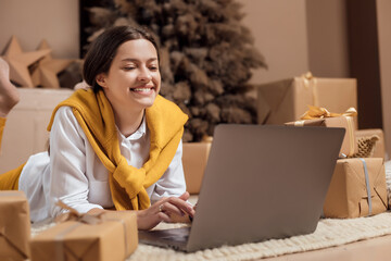 Young woman with credit card shopping online on laptop in cozy christmas interior