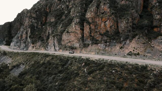 Dark grey car drives through narrow road in the mountains. Drone footage