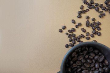 part of a black mug filled with roasted whole coffee beans stands on a beige background with coffee beans. top view