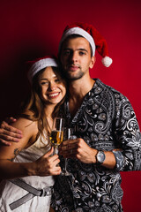 Young couple with Christmas hats and champagne glasses on red background.