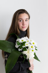 Medium vertical portrait of pretty fair teenaged girl in brown wool sweater holding bouquet of white flowers
