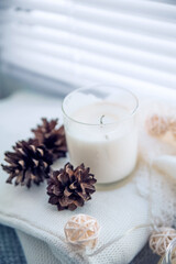 Burning candles and white sweaters on windowsill. Cozy autumn and winter concept, window with blinds...