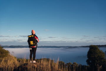 Woman hiker with backpack enjoying the foggy scenery at the top of the mountain.