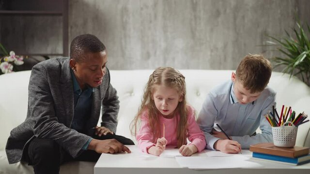 Young black English teacher writes invisible letters by finger on table and little kids guess and write at home lesson with native speaker slow motion