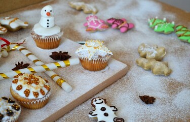 Christmas composition: Christmas cupcakes decorated with icing and surrounded by cinnamon sticks and star anise on a background of powdered sugar