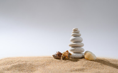 Fototapeta na wymiar White pebble pyramid with small seashells on a light gray background.