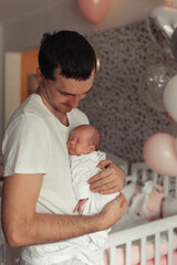 Portrait of young father holding tight newborn daughter in his arms. Lifestyle photo in bedroom. Decoration with baloons.Selective focus. Film grain