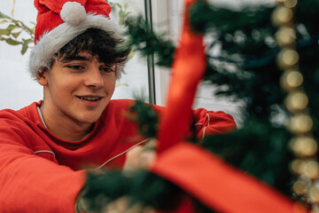 teenage boy decorating christmas tree at home with santa claus hat