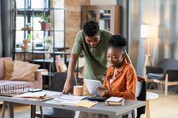 Smiling young African American couple using tablet app while planning family budget in living room