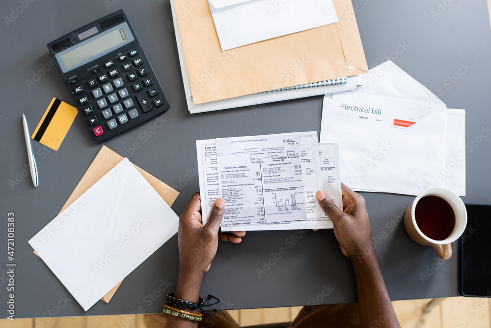 Poster Above view of unrecognizable Blackman sitting at table with letters, credit card and calculator and analyzing bills