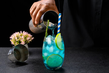 bartender serving with a cocktail shaker a blue drink in a glass decorated with rosemary, ice and...