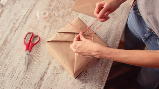 Overhead view of young woman wrapping gift box on table at home. Woman wrapping gift box