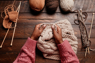 Top view close up of female hands knitting against dark wooden background, copy space - obrazy, fototapety, plakaty