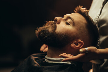 Close shot of a young man beard while he is sitting at a barbershop - obrazy, fototapety, plakaty