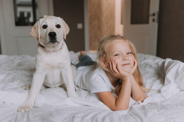 portrait of a little blonde girl lying in bed with her beloved dog in her arms. girl in a white T-shirt and jeans and a pet are lying on white bed linen. space for text. High quality photo