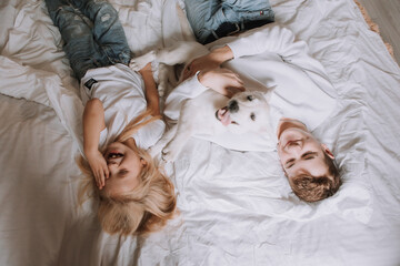 boy and a girl in white T-shirts, brother and sister are lying in a bed made with white linens with a dog. top view. favorite pet. place for text. High quality photo