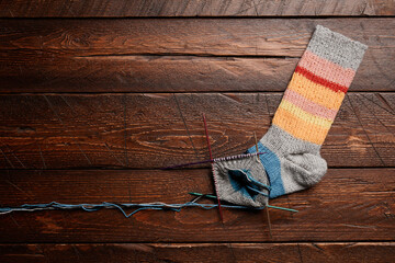 Fototapeta na wymiar Background image of unfinished knit socks on dark wooden background, knitting and hobby, copy space
