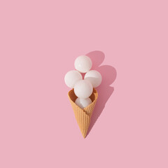 Ice cream cone with white  christmas baubles under direct light on pastel pink background. Christmas and new year celebration concept, flat lay perspective, square ratio.