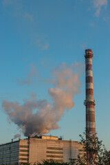 Brick chimney with white smoke over an industrial building