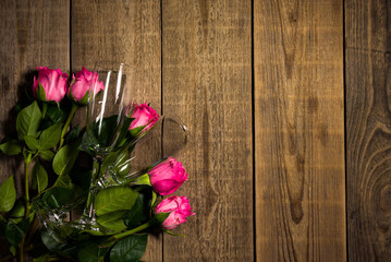 Fototapeta na wymiar Decoration for spending romantic evening together made of roses and two wine glasses. Pink flowers are lying on the wooden table filmed in closeup from above. Elegant flirting design for a lovely date
