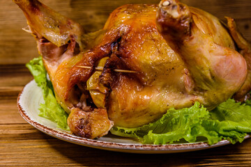 Plate with roasted whole chicken and lettuce leaves on a wooden table