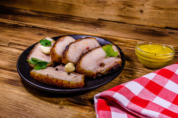 Slices of baked pork belly, garlic and parsley on a black plate