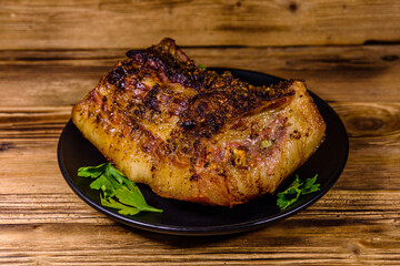 Baked piece of pork belly and parsley on a black plate