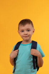 Portrait of a handsome little smiling boy. Adorable small child smiles on yellow background.a boy with a school backpack behind his back