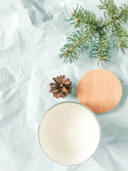 White aromatic candle with spruce branch and pine cone on the blue textural background.