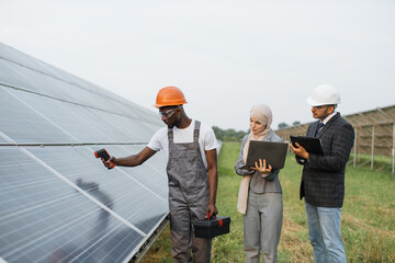 African american technician showing temperature of solar panels on thermal imager to muslim woman...