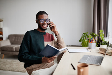 Portrait of young African-American man wearing glasses while working from home and speaking by...