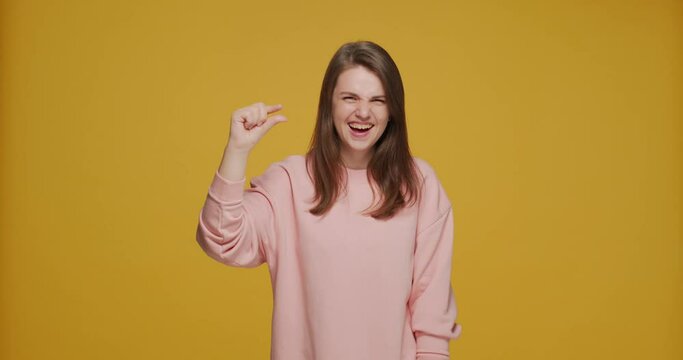 Joyful laughing young girl showing little bit gesture tiny size by finger. Small prices or rates and sale concept