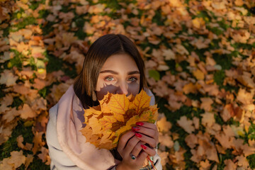 cute brunette in a beige coat with leaves in her hands on a background of autumn leaves