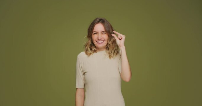Giggling young girl showing with fingers small prices gesture enjoying sale and discount on green studio background