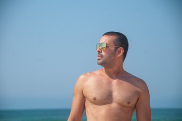 handsome athletic man on vacation, wearing sunglasses admiring the scenery on the beach on a sunny day.