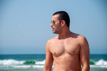 handsome athletic man on vacation, wearing sunglasses admiring the scenery on the beach on a sunny day.