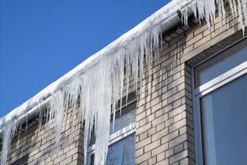 Fototapeta premium Bright sunny day. Long, shiny icicles on the roof of the house. Frosty morning. Dangerous place of falling icicles.