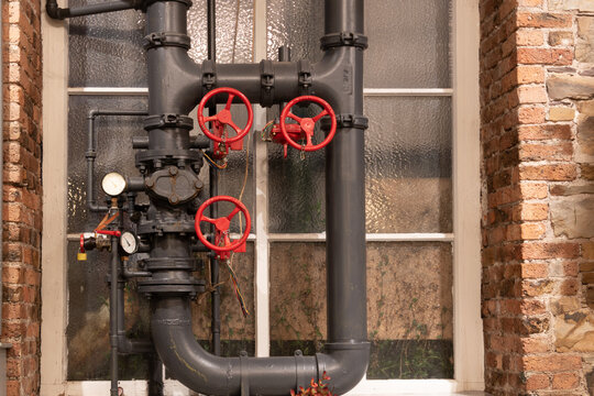 Vintage steam pipes and valves with gages against old window.