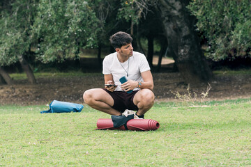 Man using a mobile squatting next to a yoga mat outdoor