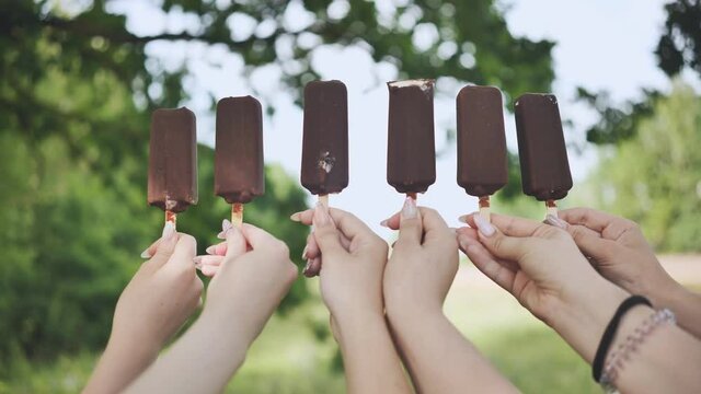 Friends hold chocolate ice cream on a stick in a row.