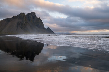 Sunrise Stokksnes cape sea beach and Vestrahorn Mountain with its reflection on wet black volcanic sand surface, Iceland. Amazing nature scenery, popular travel destination.