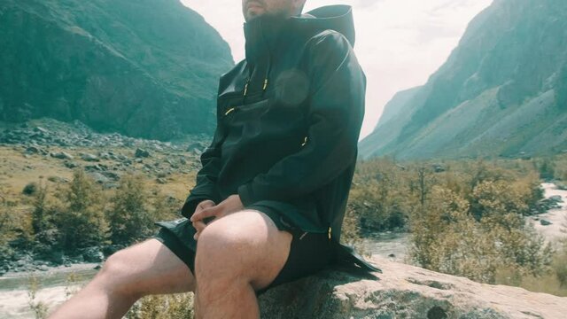 A man sits on the edge of a cliff wearing a black anorak. Katu-Yaryk canyon Chulyshman Valley. Altai